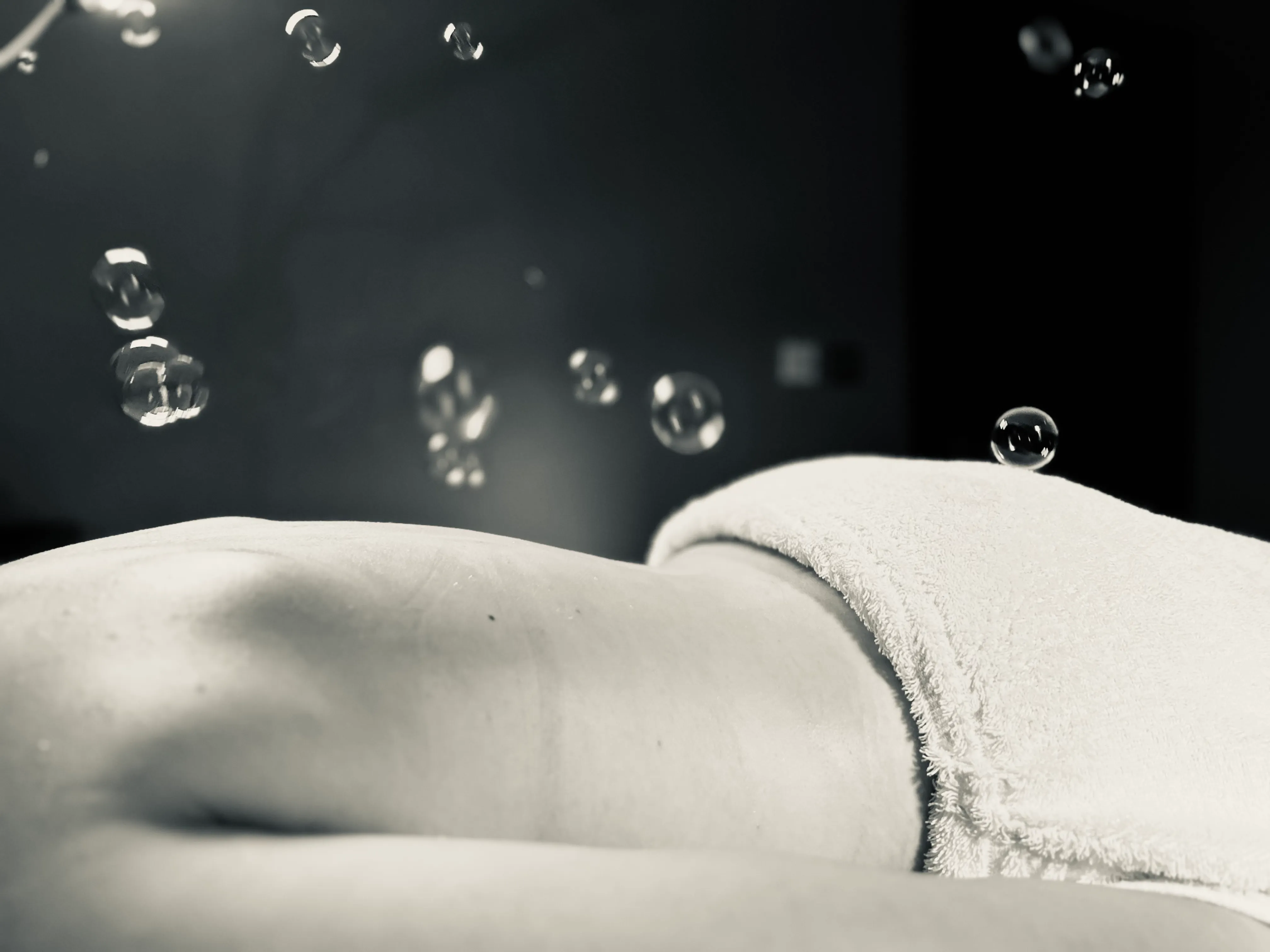 Soft bubbles drifting gently above resting skin in low light, evoking the light, adapted touch of oncology touch therapy at Artemis Therapies