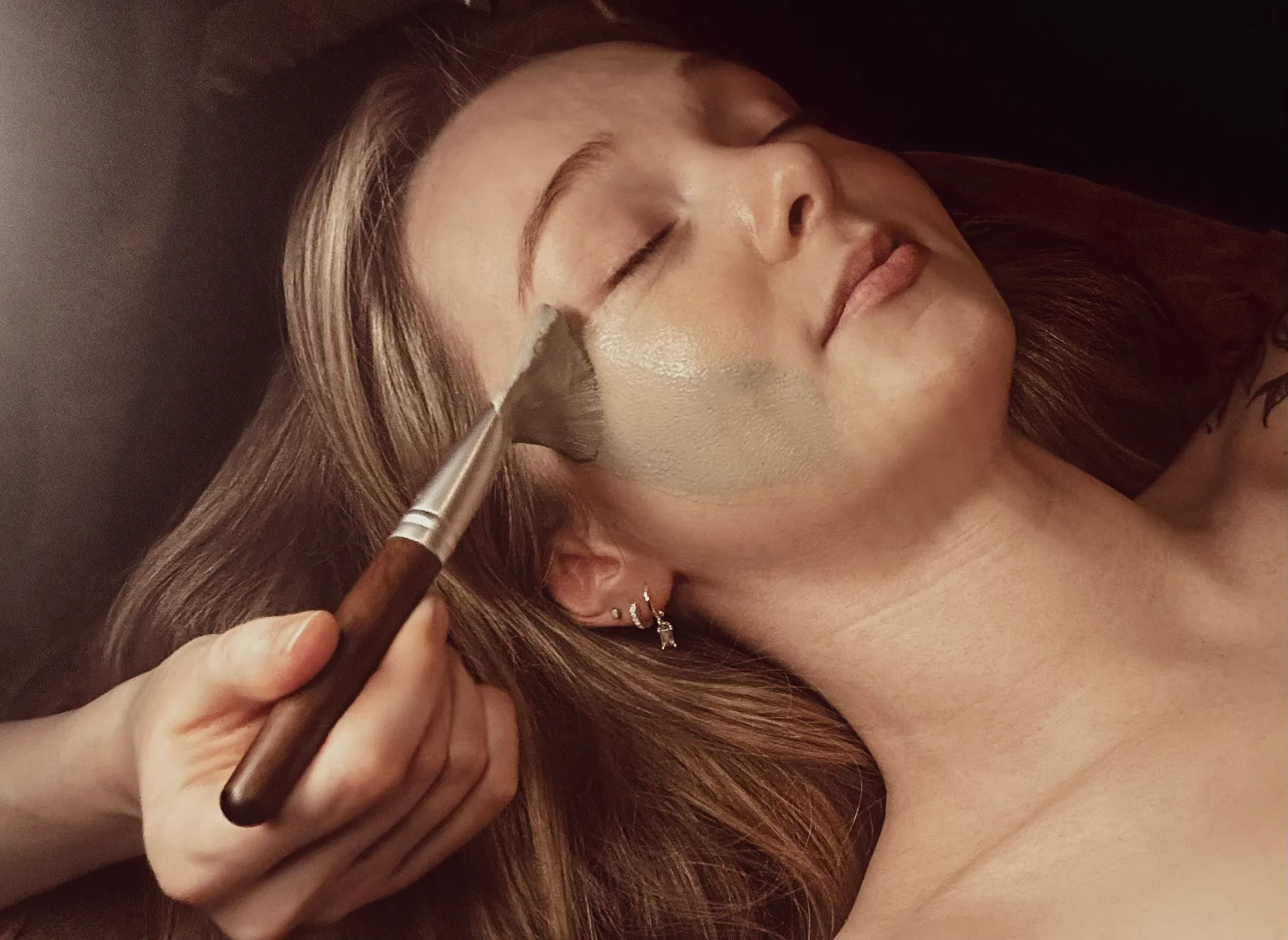 A botanical clay mask being brushed gently onto the face during a facial ritual at Artemis Therapies in Ruthin