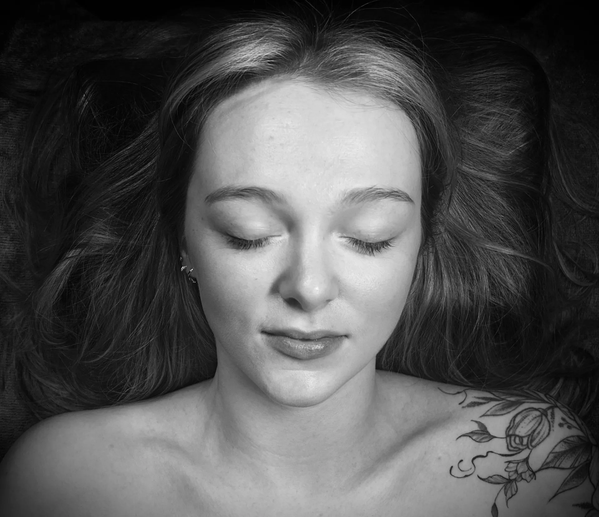A soft black and white portrait of a client resting calmly, eyes closed, during a treatment at Artemis Therapies