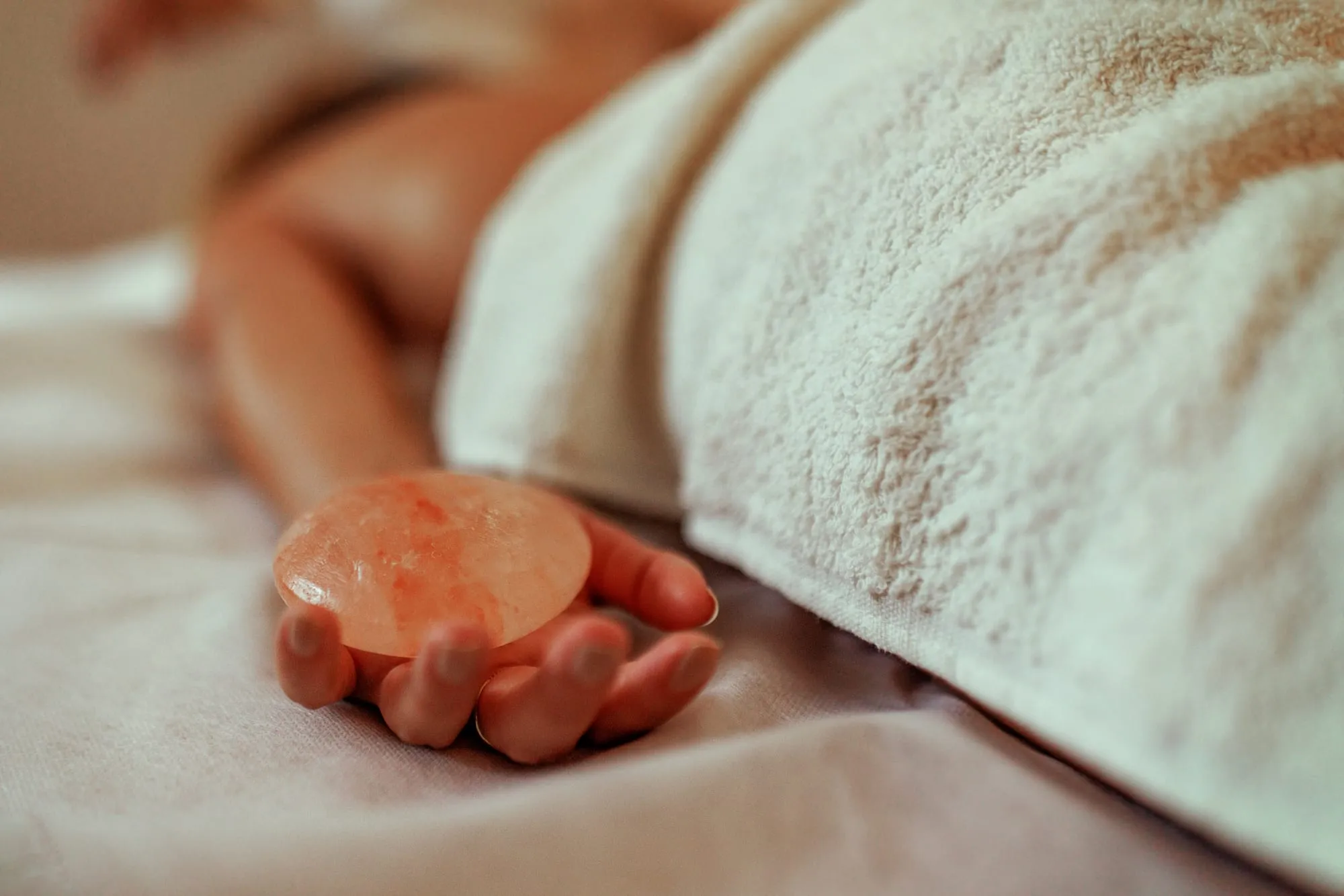 A warm Himalayan salt stone resting in an open hand beside a soft towel at Artemis Therapies